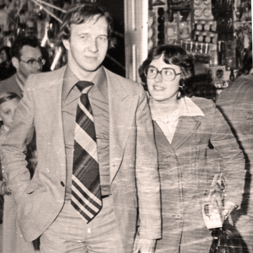 Een zwart-witfoto van een man en vrouw in jaren '70-stijl kleding, lopend in een winkelstraat.