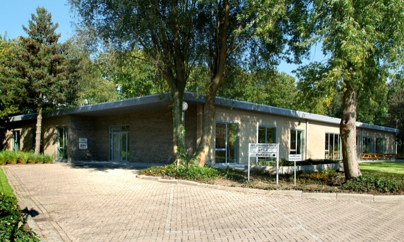 Nieuwbouw kantoor omgeven door bomen en plaveisel, ideaal voor creatieve uitgeverijprocessen.