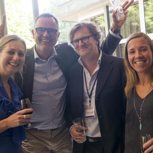 Groep mensen glimlachend op een uitgeversevenement, met drankjes in de hand.