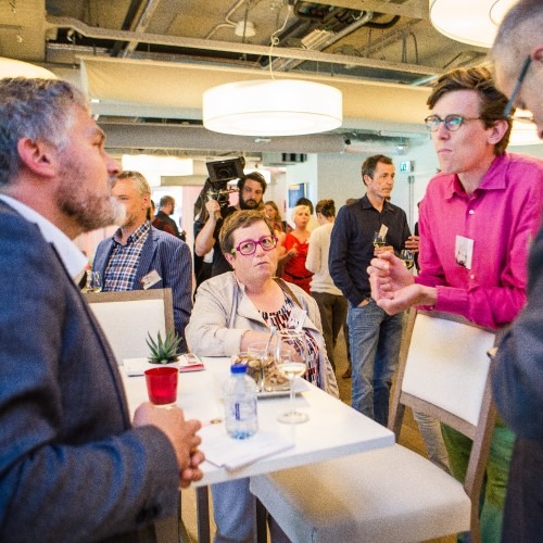 Groep mensen in gesprek tijdens een netwerkevenement in een moderne ruimte met tafels en stoelen.