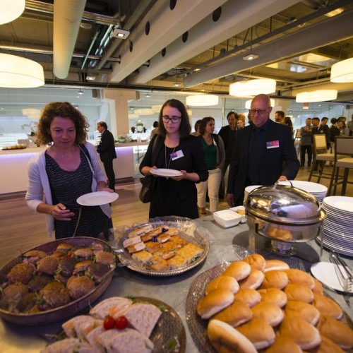 People getting food at a buffet with bread and sandwiches during an event.