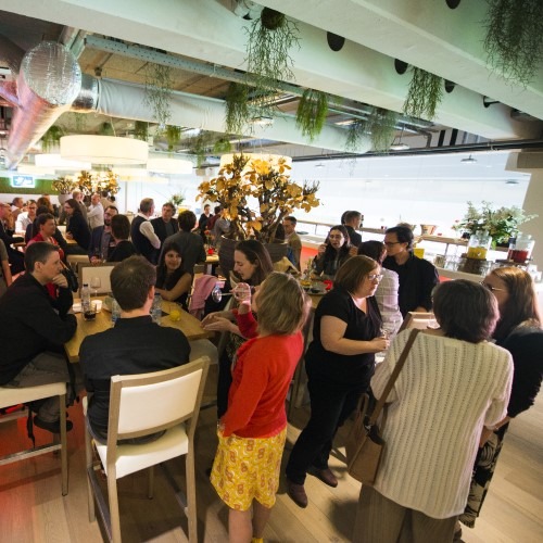 Een gezellige bijeenkomst van mensen in een modern kantoor met planten en diverse zitplekken.