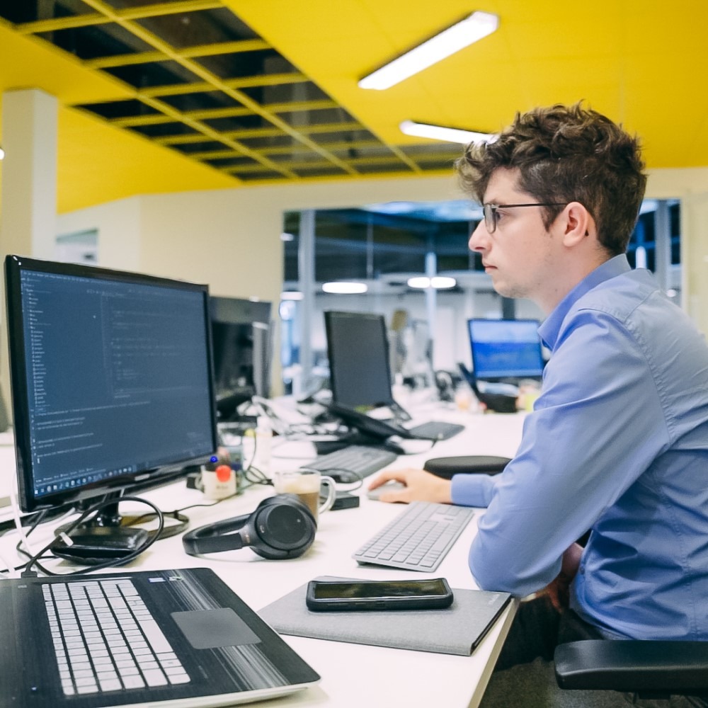Man werkt geconcentreerd aan computer in modern kantoor, omringd door technologie.