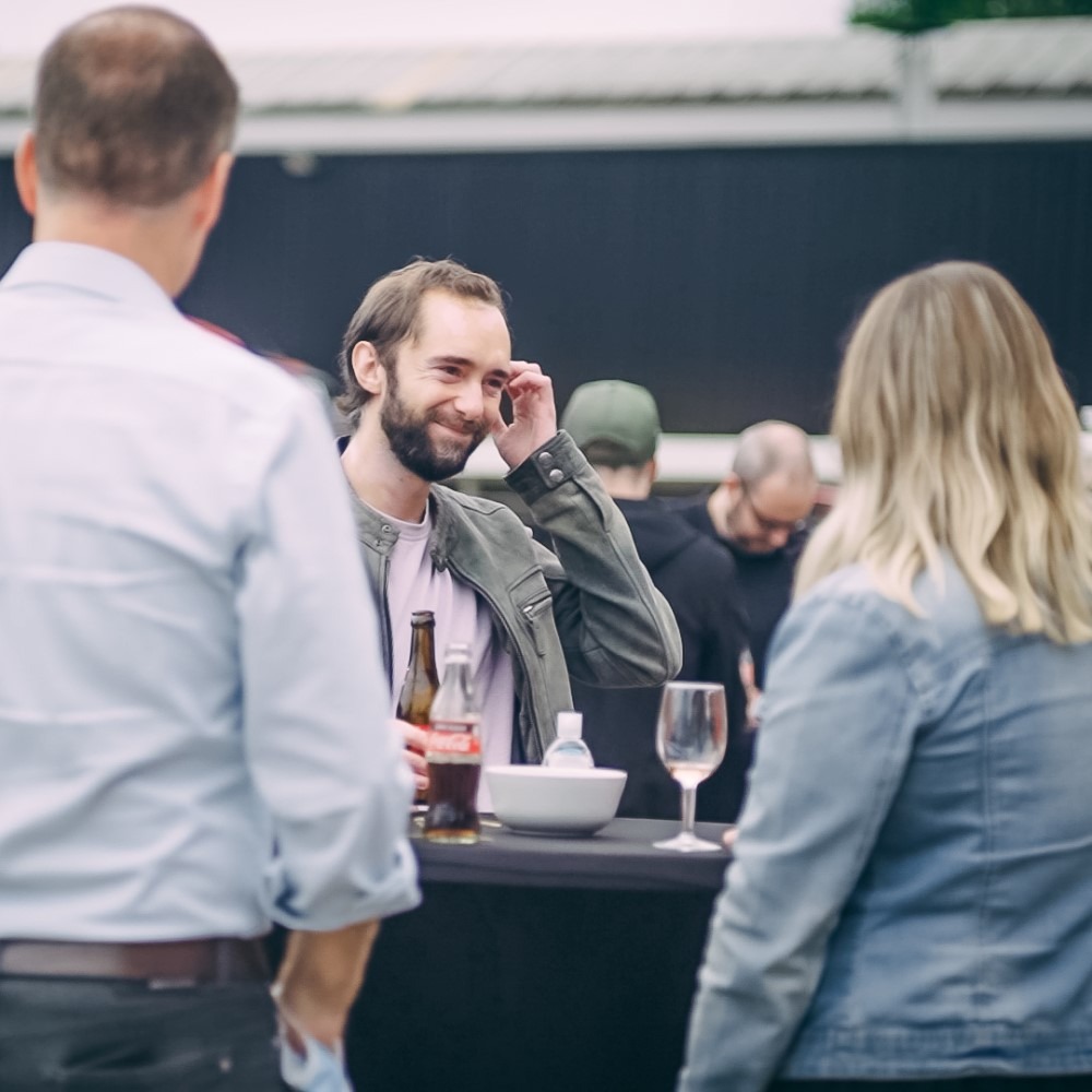 Mensen in gesprek bij een statafel met drankjes tijdens een netwerkbijeenkomst.