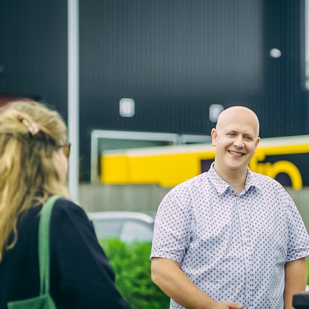 Twee mensen in gesprek buiten bij een gebouw, de man glimlacht.