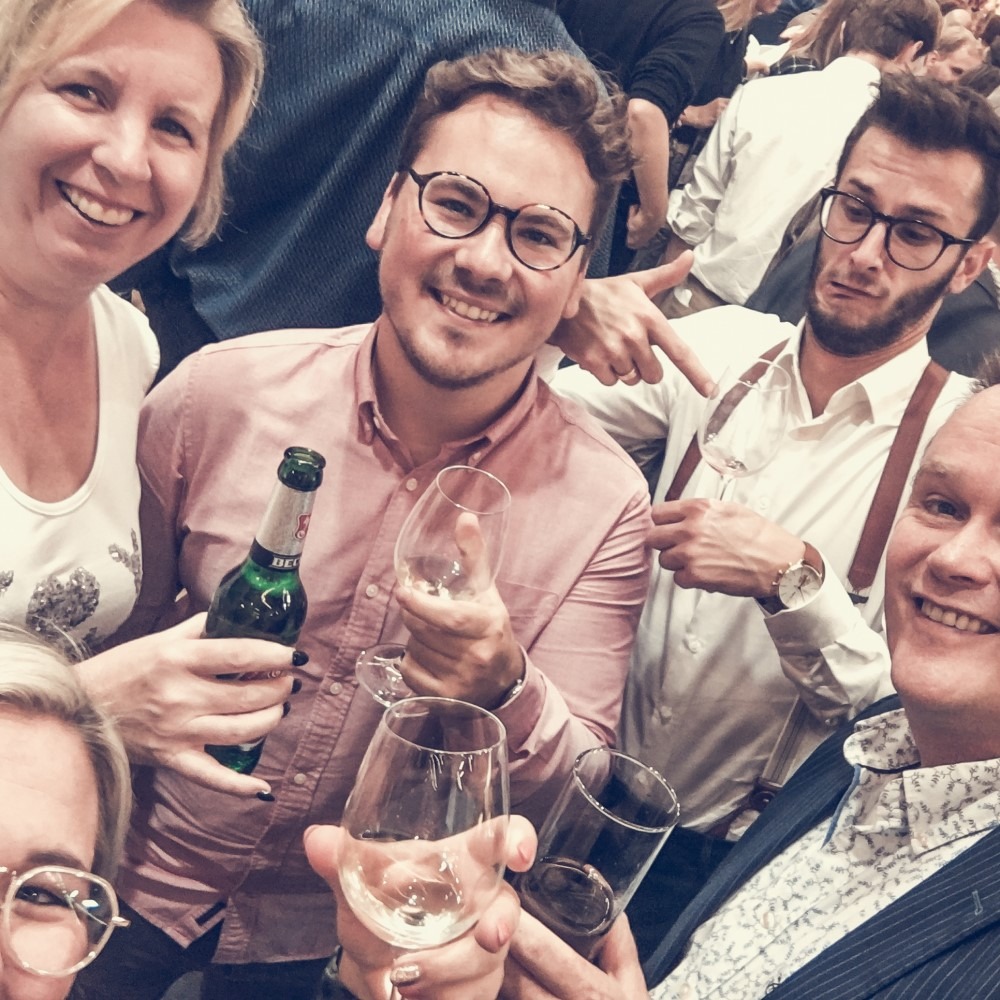 Groep collega's tijdens een evenement met drankjes en lachende gezichten.