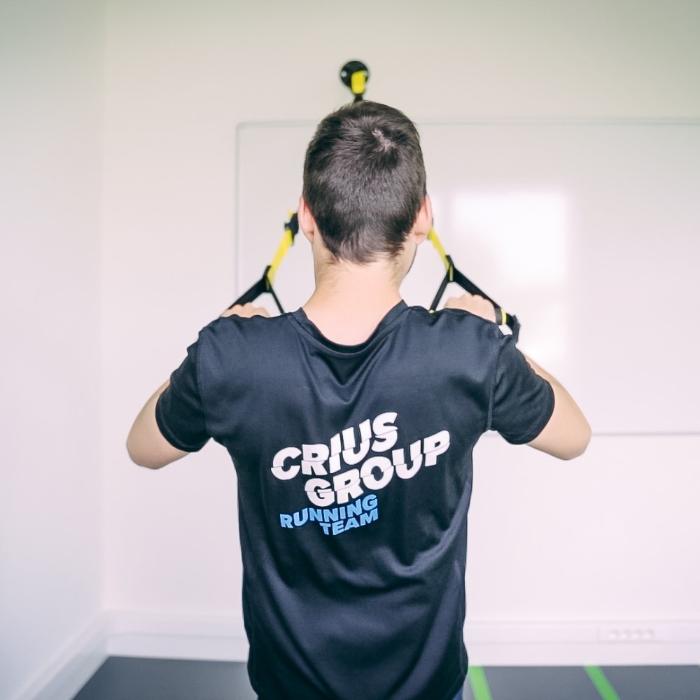 Persoon in Crius Group shirt traint met weerstandsbanden in een lichte ruimte.