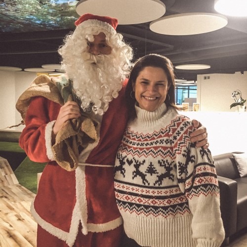 Persoon in kersttrui poseert met kerstman in kantooromgeving.