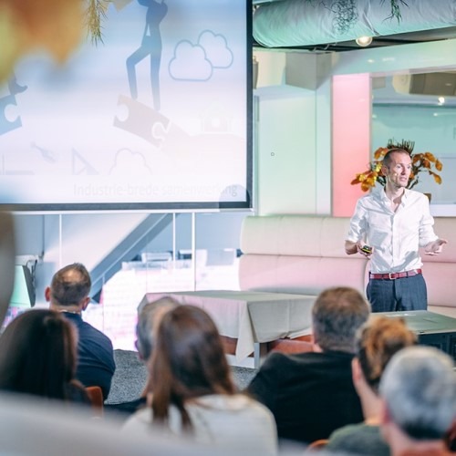 Presentation in a modern space with a speaker in front of an audience and a projected screen.