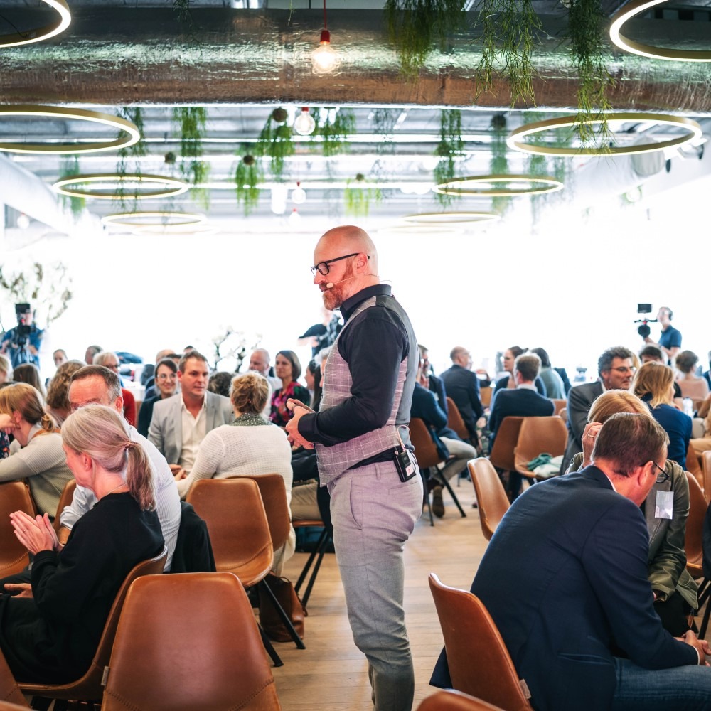People in a well-lit room sitting and standing by tables during a meeting or conference.