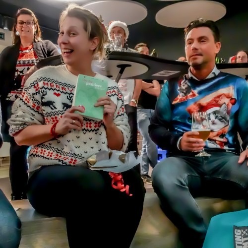 Groep mensen in kersttruien glimlacht en houdt drankjes vast tijdens een bijeenkomst.