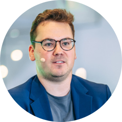 Portrait of a man with glasses and a blue jacket, looking forward in a professional setting.