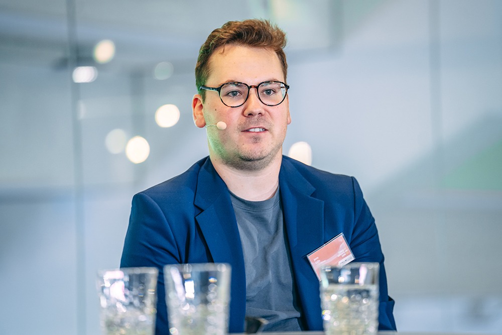 Man met bril en donkerblauw jasje zit aan tafel met glazen water.