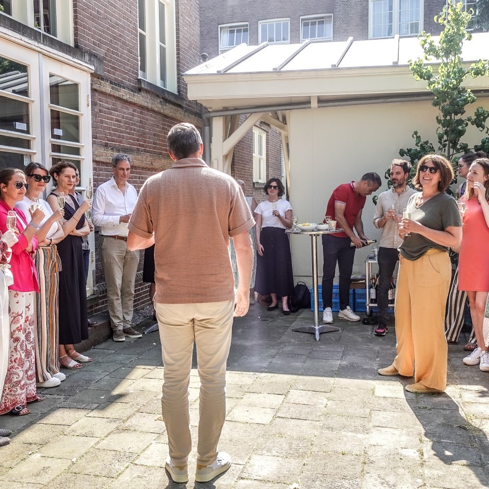 A group of people standing outside at an event, conversing and enjoying the weather.