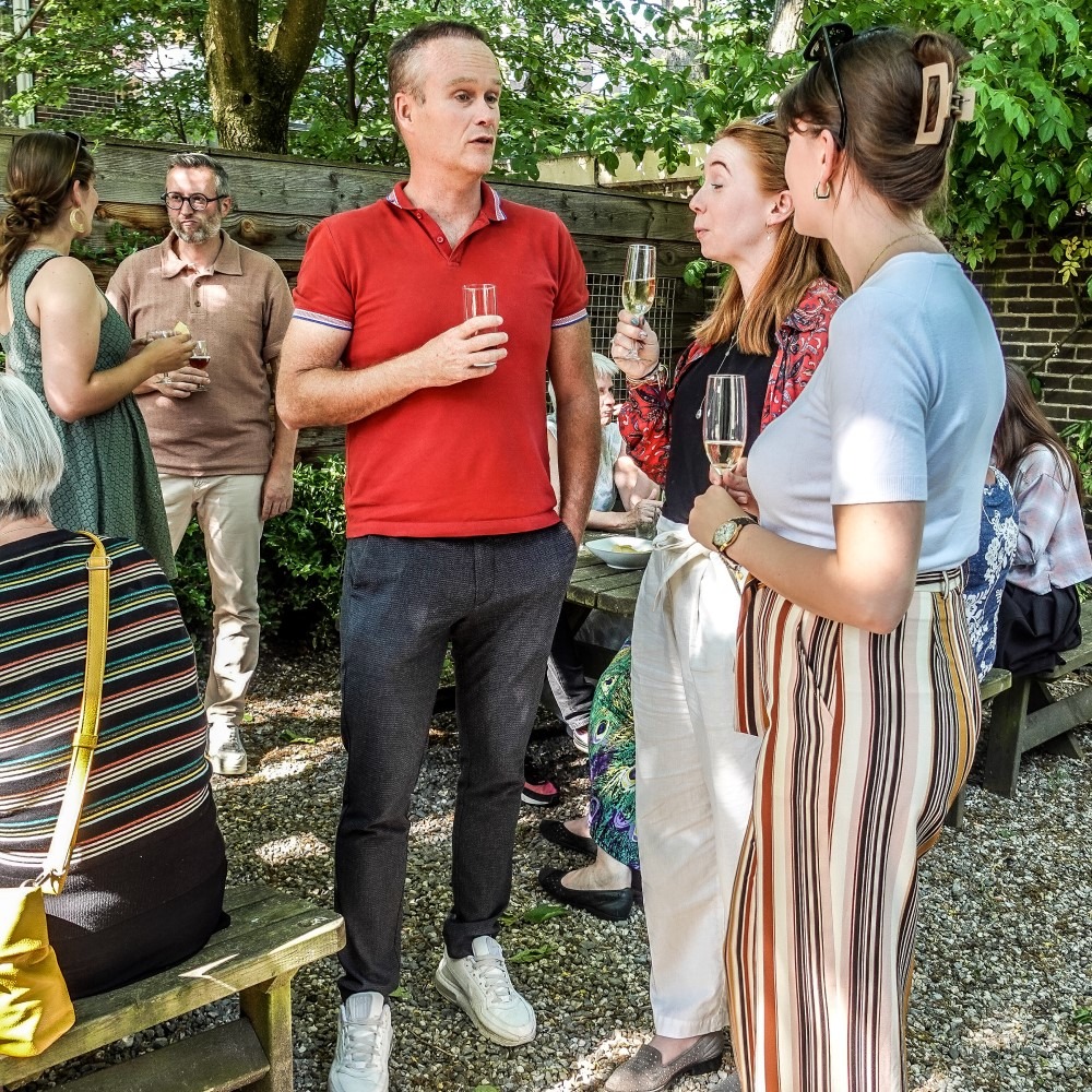 People talking and drinking in a garden during an informal event.