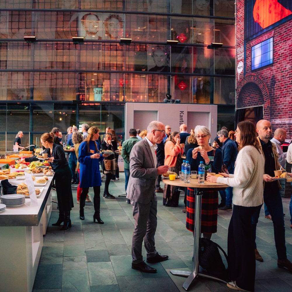 Mensen netwerken tijdens een evenement met hapjes in een grote, sfeervolle zaal.