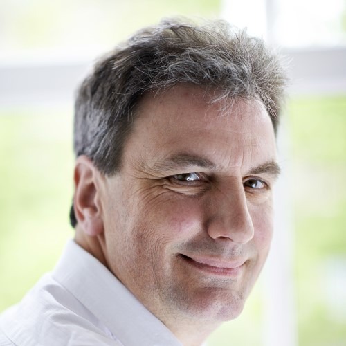 Portret van een lachende man in een witte blouse voor een raam, gefocust op uitgeverij-optimalisatie.