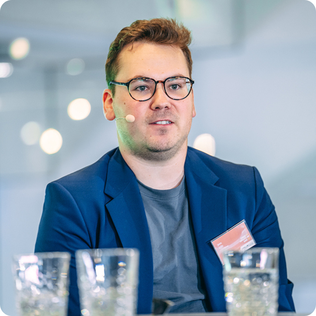 Man in blauwe blazer zit aan tafel met glazen op de voorgrond.