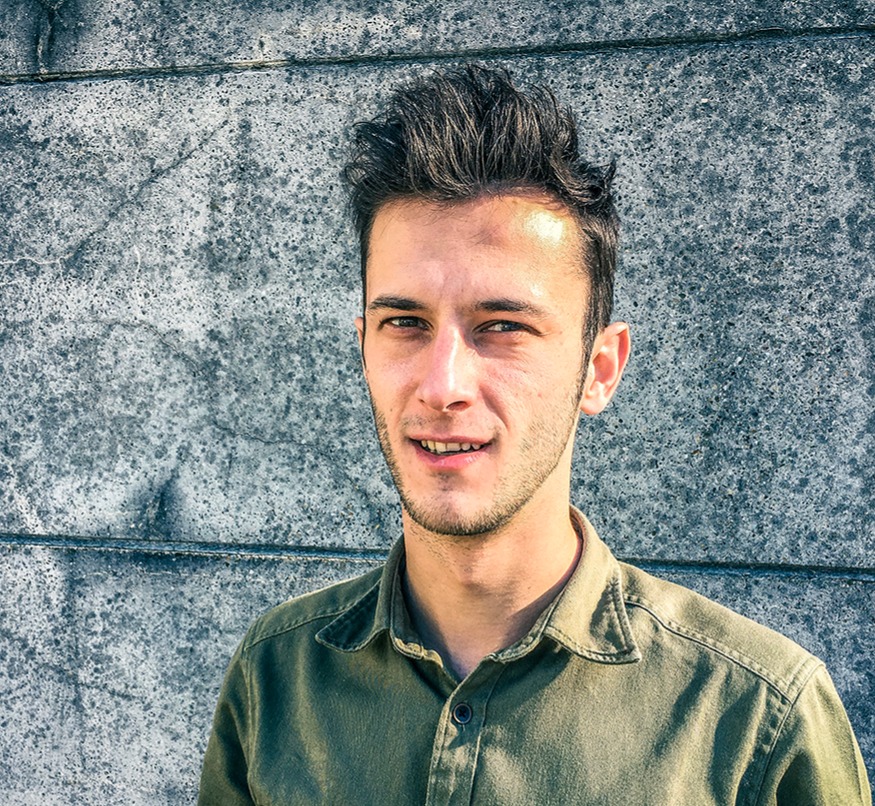 Man met groene overhemd voor een stenen muur.